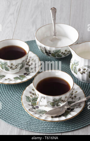 Tazza di tè sul piattino con cucchiaino bricco per il latte e lo zucchero ciotola su un cartellone verde grigio con superficie di legno Foto Stock