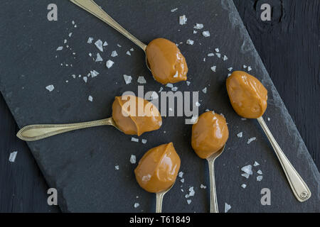 Cucchiai di caramello con sale a scaglie su nero ardesia sfondo Foto Stock