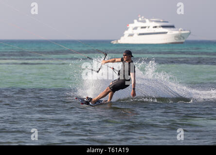 Un kiteboarder indossa tutto nero a calci fino a spruzzo enorme davanti a un grande yacht a motore. Foto Stock