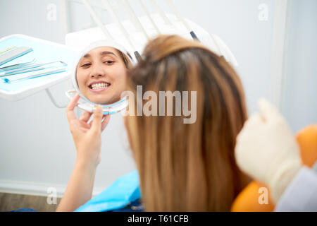 Donna che guarda nello specchio dopo lo sbiancamento dei denti Foto Stock