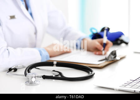 Primo piano dello stetoscopio. Medico donna riempie la forma medica mentre seduto alla scrivania in ospedale. Sanità, Workplace e cardiologia in medicina Foto Stock