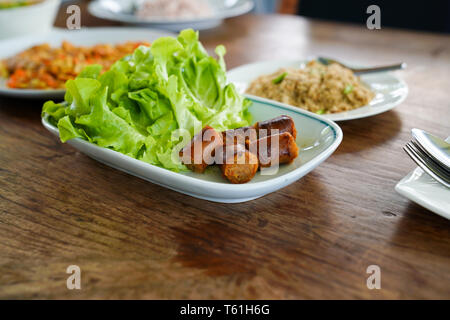 Affettato Notrhern Thai salsiccia piccante 'Sia Aua' sulla piastrella bianca disco, decorare dalla quercia verde. Foto Stock