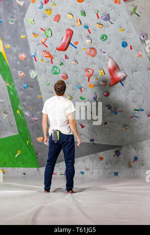 Rocciatore si alza e guarda la parete di arrampicata con ganci in boulder hall Foto Stock