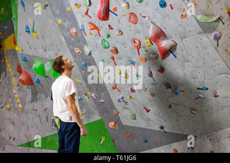 Rocciatore si alza e guarda la parete di arrampicata con ganci in boulder hall Foto Stock