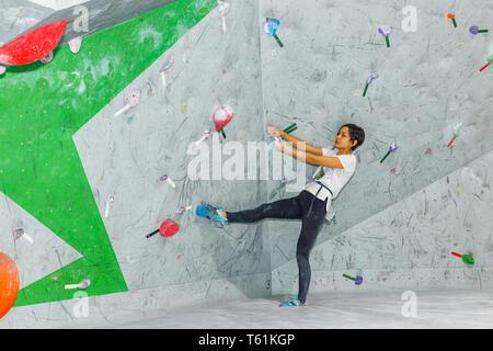 Rocciatore donna appeso su un bouldering parete di arrampicata, all'interno sui ganci colorati Foto Stock