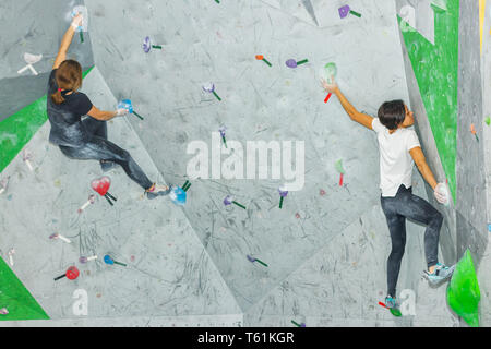 Rocciatore donna appeso su un bouldering parete di arrampicata, all'interno sui ganci colorati Foto Stock