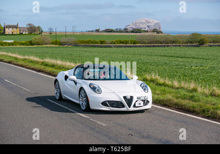 East Lothian, Regno Unito. Il 28 aprile 2019. Classic Car Tour: North Berwick Rotary Club mantiene la sua 3° rally con 65 classic le vetture iscritte. La vettura da rally è percorso da East Lothian e indietro attraverso i confini Scozzesi, la raccolta di fondi per le associazioni di beneficenza locali. Un 2017 Alfa Romeo 4C convertibile auto sportive con Bass Rock gannet colonia di Firth of Forth Foto Stock