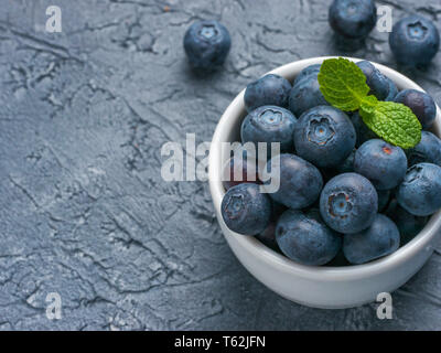 Appena raccolti i mirtilli closeup. Mature e succose ai mirtilli freschi con verde menta sulla texture di sfondo di calcestruzzo. Mirtillo nero su sfondo grigio con copyspace. Vista superiore o laici piatta Foto Stock