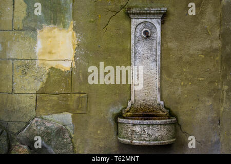 Vecchio vintage acqua potabile fontana appeso ad un muro di pietra, storico alla ricerca di oggetti Foto Stock