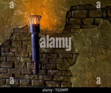 Vecchio cercando e illuminati torcia in metallo appeso ad un muro di pietra, medievale interni Foto Stock