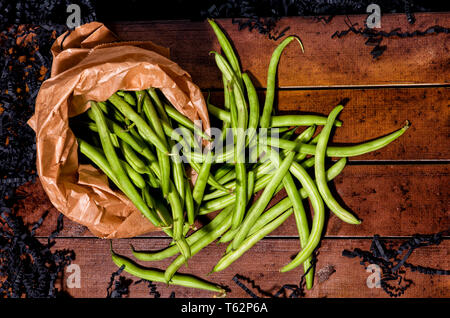 Fagiolini freschi in un sacchetto di carta giacente su di una superficie di legno Foto Stock