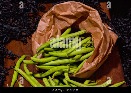 Fagiolini freschi in un sacchetto di carta giacente su di una superficie di legno Foto Stock