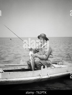 1920s uomo BARNEGAT BAY pescatore commerciale seduti in barca d'anatra fumatori la rimozione della tubazione FISHHOOK dalla cattura di pesci NEW JERSEY USA - Una143 HAR001 HARS B&W uomo di mezza età successo attività di specialità CANVAS DIVERTIMENTI HOBBY INTERESSE rimozione hobby passatempo conoscenza piacere NJ OCCUPAZIONI DUCK BOAT CANNA DA PESCA NEW JERSEY vecchia salina OILSKIN CERATA AMATORIALE DI RILASSAMENTO BARNEGAT BAY in bianco e nero di etnia caucasica GODIMENTO HAR001 in vecchio stile Foto Stock