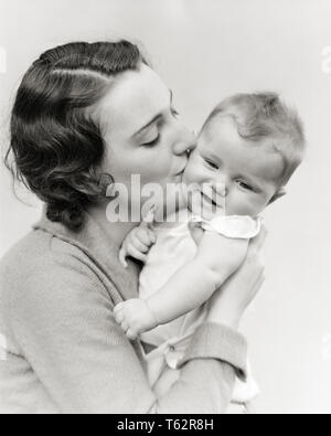 1930s BRUNETTE DONNA MADRE HOLDING abbracciando baciando la guancia di sorridere SQUIRMING BABY Figlio bambino - b12053 HAR001 HARS OLD FASHION 1 trattamento viso giovanile adulti giovani e LAVORO DI SQUADRA FORTE PER NEONATI FIGLI LIETA GIOIA LIFESTYLE FEMMINE HOME VITA ONOREVOLI PERSONE CARING ESPRESSIONI MASCHI B&W BRUNETTE felicità testa e spalle allegro del sorriso gioioso baby boy attaccamento personale affetto emozione novellame mamme RELAX SQUIRMING convivere giovane donna adulta in bianco e nero di etnia caucasica HAR001 in vecchio stile Foto Stock