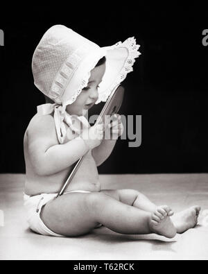 1940s BABY indossando cofano cercando in mano specchio - b18677 HAR001 HARS concettuale cofani elegante idee di crescita novellame specchi riconoscere immagine di sé bambina in bianco e nero di etnia caucasica HAR001 VECCHIO VANA Foto Stock