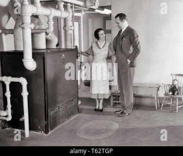 1920s 1930 orgoglioso uomo donna che guarda la nuova fornace di riscaldamento nel seminterrato - ho1085 HAR001 HARS HOME VITA DI LUSSO spazio copia amicizia a lunghezza piena RISCALDATORE LADIES persone maschi residenziale edifici fiducia B&W PARTNER indossare giacca e cravatta felicità seminterrato orgoglio case residence elegante casa MIGLIORAMENTO MID-adulto metà uomo adulto a metà donna adulta soluzioni mogli convivere in bianco e nero di etnia caucasica HAR001 in vecchio stile Foto Stock