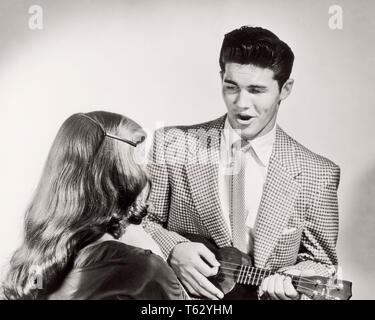 Anni Cinquanta giovane uomo che indossa indossare giacca e cravatta cantando la riproduzione di UKULELE PER DONNA VISTO DA DIETRO - m1825 CLE003 HARS LADIES PERSONE ISPIRAZIONE MASCHI ENTERTAINMENT B&W indossare giacca e cravatta felicità alto angolo e acconciatura canzone VOCAL VISTA POSTERIORE INTRATTENITORE STRUMENTO MUSICALE collegamento concettuale di eseguire vocalizzi vocals capelli lunghi brani elegante UKULELE VISTA POSTERIORE creatività convivere giovane uomo adulto giovane donna adulta in bianco e nero di etnia caucasica in vecchio stile Foto Stock