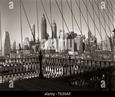 Anni Cinquanta skyline di Manhattan visto attraverso i cavi del ponte di Brooklyn New York City NY USA - R823 RCH001 HARS grattacieli in sospensione Foto Stock