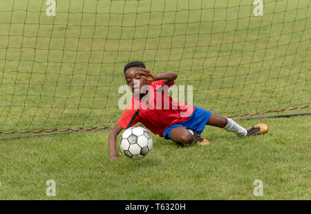 Hampshire, Inghilterra, Regno Unito. Aprile 2019. Un giovane giocatore di football per difendere l'obiettivo durante una sessione di formazione in un parco pubblico. Foto Stock