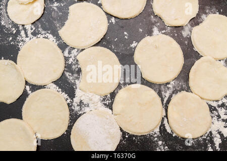 Arrotolate l'impasto crudo tagliato in roundels su una tabella con farina diffusa Foto Stock