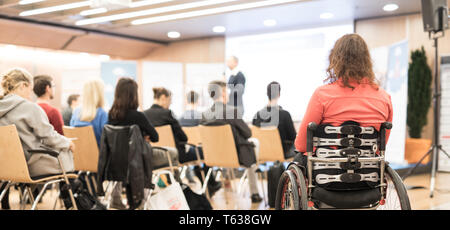 Vista posteriore di un irriconoscibile donna su una sedia a rotelle che partecipano a conferenze di affari parlare. Foto Stock