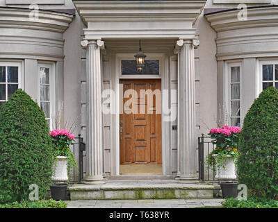 Parte anteriore del paesaggistico elegantemente casa in pietra con portico di colonne in legno porta anteriore Foto Stock