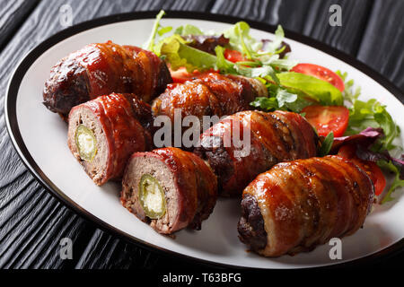 Deliziosa Armadillo uova ripiene con jalapeno e formaggio avvolto in pancetta servito con insalata fresca close-up su una piastra sul tavolo orizzontale. Foto Stock