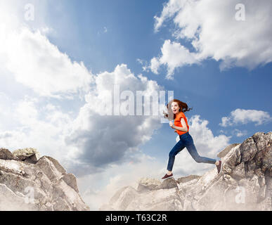 Redhead donna salta alla scogliera sul cielo blu sullo sfondo. Foto Stock