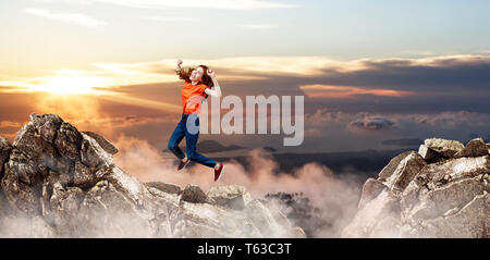 Redhead donna salta alla scogliera sul cielo blu sullo sfondo. Foto Stock