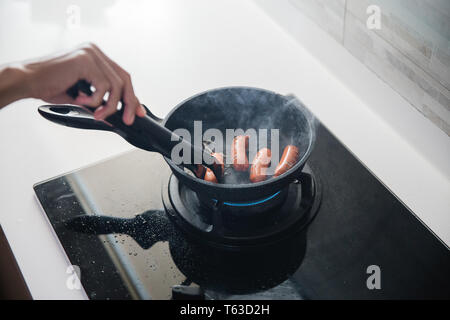 Mani con pinze da alimentare alla frittura salsicce Foto Stock