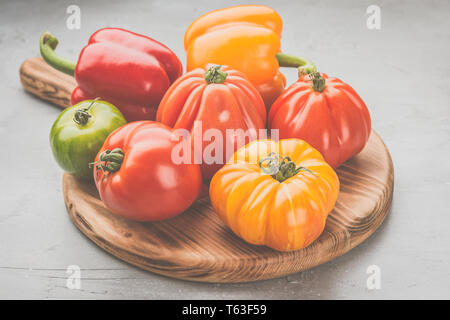 Selezione di grandi organici cimelio di pomodori e peperoni sul pannello di legno, sul cemento grigio sfondo, il fuoco selettivo Foto Stock