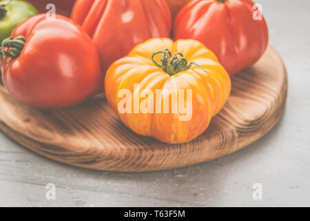 Selezione di organico cimelio di grandi pomodori close up sul pannello di legno, sul cemento grigio sfondo, il fuoco selettivo Foto Stock