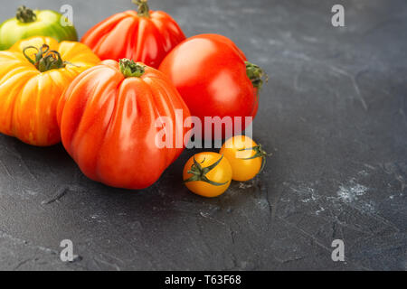 Selezione di organico cimelio di grandi dimensioni e i pomodori ciliegia vicino sul blu scuro dello sfondo concreto, il fuoco selettivo Foto Stock