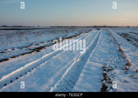 Le tracce delle ruote su una strada innevata, Horizon e sky - vista invernale Foto Stock