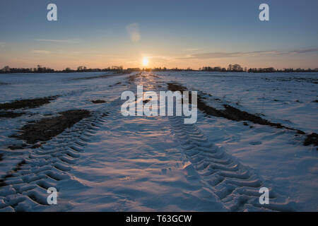 Le tracce delle ruote su un snowy strada sterrata, orizzonte e tramonto - vista invernale Foto Stock