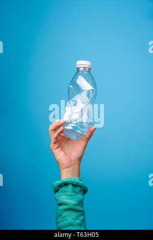 La bottiglia di plastica in mano contro sfondo blu. Foto Stock