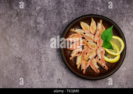 Piatto di gamberi di mare bolliti con limone su una piastra su un sfondo scuro Foto Stock