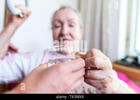 Una giovane donna dà un bicchiere di acqua ad una vecchia donna Foto Stock
