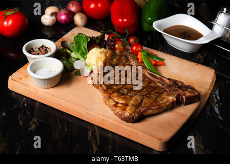 Grigliata di grandi t-bone steak guarnita con erbe aromatiche, il pomodoro e il sale Foto Stock