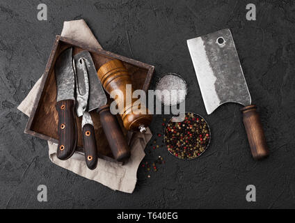 Carne Vintage coltello e forchetta e ascia di guerra nella vecchia scatola di legno nero su sfondo tabella. Butcher utensili. Foto Stock