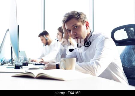 Preoccupato o stanco uomo d affari con cuffia lavorando sul computer in ufficio. Foto Stock