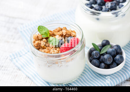 Un vasetto di yogurt con granola e bacche blu sul tessile, primo piano. Pulire il concetto di mangiare Foto Stock