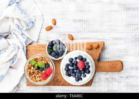 Yogurt con frutti di bosco e granola in barattolo, table top vista sul bianco sullo sfondo di legno. Copia spazio per il testo Foto Stock