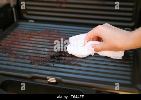 Sporco grill elettrico. Femmina di tergitura a mano con un panno grill. Foto Stock