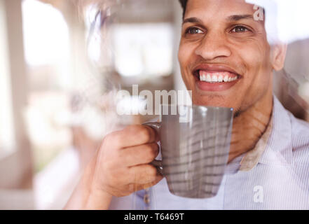 Ritratto di ispanico uomo con un bicchiere di acqua al chiuso in casa, guardando fuori della finestra. Shot attraverso il vetro. Foto Stock