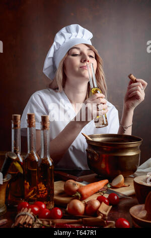 Giovane donna in chef uniforme con piccole bottiglie di olio vegetale. Fragrante olio di oliva con varie spezie e erbe aromatiche. Foto Stock