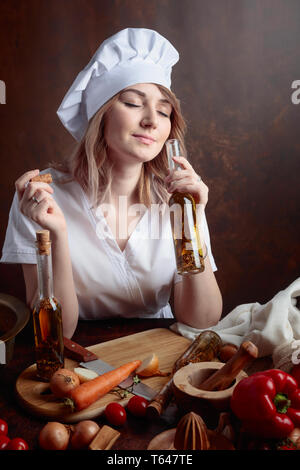 Giovane donna in chef uniforme con piccole bottiglie di olio vegetale. Fragrante olio di oliva con varie spezie e erbe aromatiche. Foto Stock