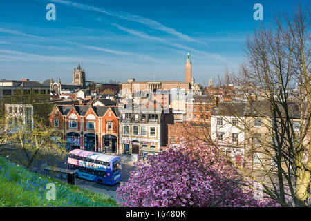 Norwich skyline della città con le sue guglie di St Peter Mancroft chiesa e della torre del municipio e autobus turistico passando da, visto dalla collina del castello. Norfolk, Regno Unito. Foto Stock