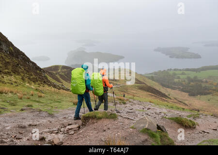 West Highland Way gli escursionisti a piedi verso il Loch Lomond e scendendo dalla collina conica in condizioni di tempo piovoso, Scotland, Regno Unito Foto Stock