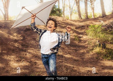 Allegro ragazzo in esecuzione in discesa con un aquilone in mano. Felice ragazzo volare un aquilone nella foresta. Foto Stock